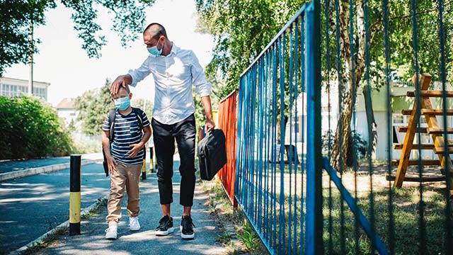 Father and son in masks walking to school